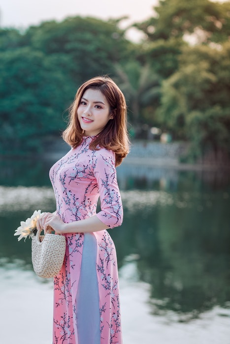 A pretty girl in pink dress posing by a lake